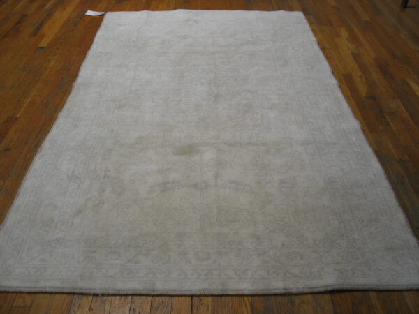 Light taupe low-pile rug with a faint border design displayed on glossy brown wood plank flooring.