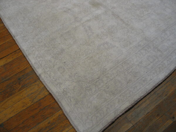 A shaggy pale gray rug with a subtle border pattern lies on distressed wooden flooring.