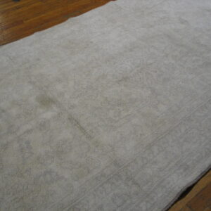 Distressed off-white rug with faint patterning rests on shiny, aged wood plank flooring.