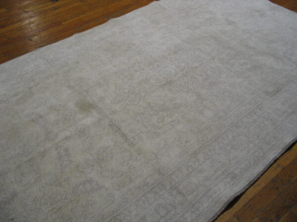 Distressed off-white rug with faint patterning rests on shiny, aged wood plank flooring.