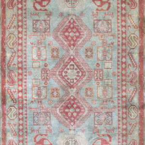 Muted blue area rug covered in traditional geometric red motifs, centered by large diamond medallions.