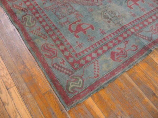 A faded teal rug with dark red geometric patterns lies on a light brown wood floor.