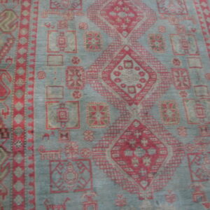 Distressed teal-gray rug featuring red tribal medallions and geometric borders lying on a wood floor.