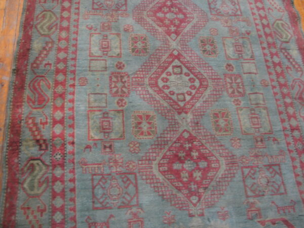 Distressed teal-gray rug featuring red tribal medallions and geometric borders lying on a wood floor.