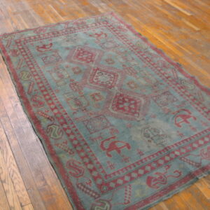 Low-pile rug in dusty blue and maroon with repeating tribal motifs over plank hardwood flooring.