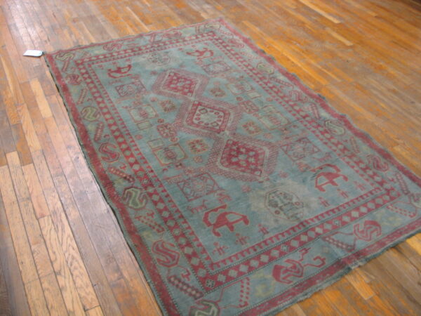 Low-pile rug in dusty blue and maroon with repeating tribal motifs over plank hardwood flooring.
