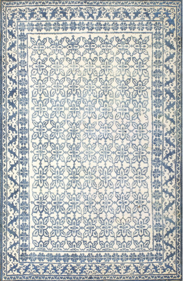 Ivory rug with a repeating distressed blue floral pattern enclosed by multiple dark blue borders.
