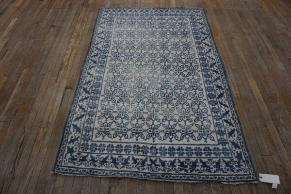 Indigo and cream rug with repeating floral medallions and complex borders on rustic wood floor.