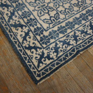 Blue and off-white patterned rug corner with visible fringe lays on distressed hardwood flooring.