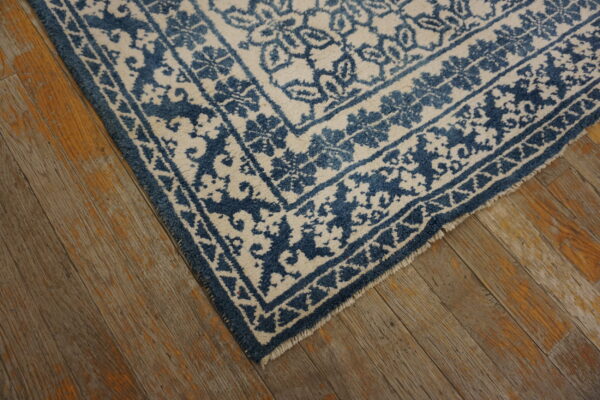 Blue and off-white patterned rug corner with visible fringe lays on distressed hardwood flooring.