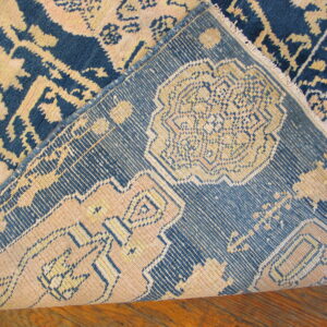 A high-pile blue and beige patterned rug is folded, revealing the detailed backing on a wood floor.