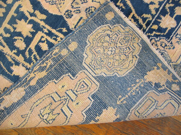 A high-pile blue and beige patterned rug is folded, revealing the detailed backing on a wood floor.