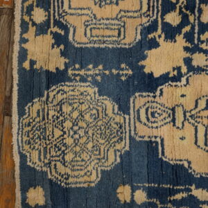 Faded patterned rug in navy blue and rust red centered on light brown wood plank flooring.