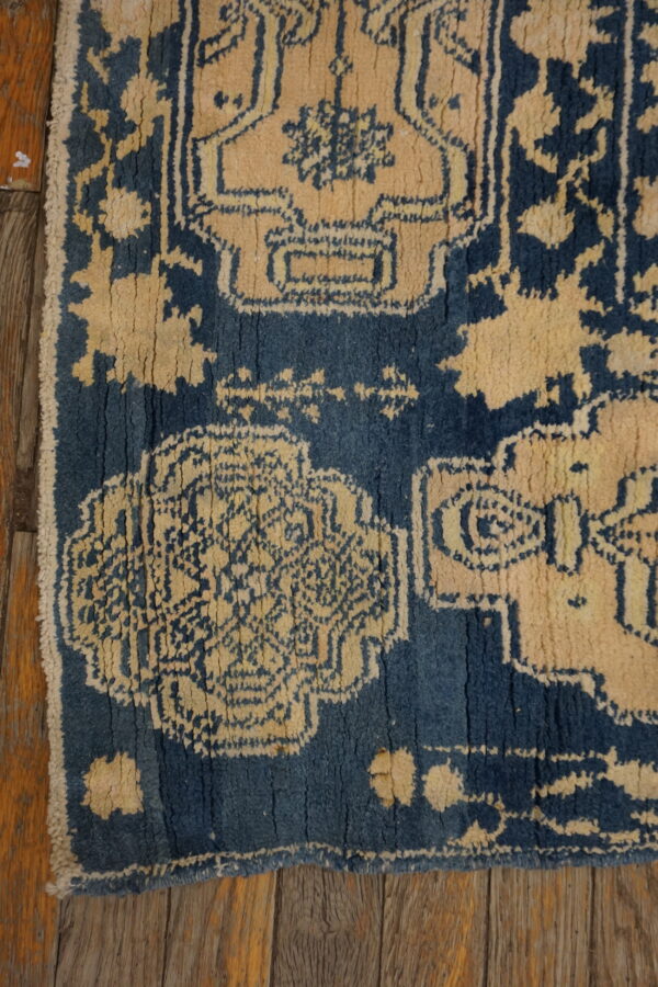 Faded patterned rug in navy blue and rust red centered on light brown wood plank flooring.