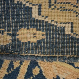 Dark blue and cream patterned rug on worn wood floors next to an inventory tag and a black shoe.