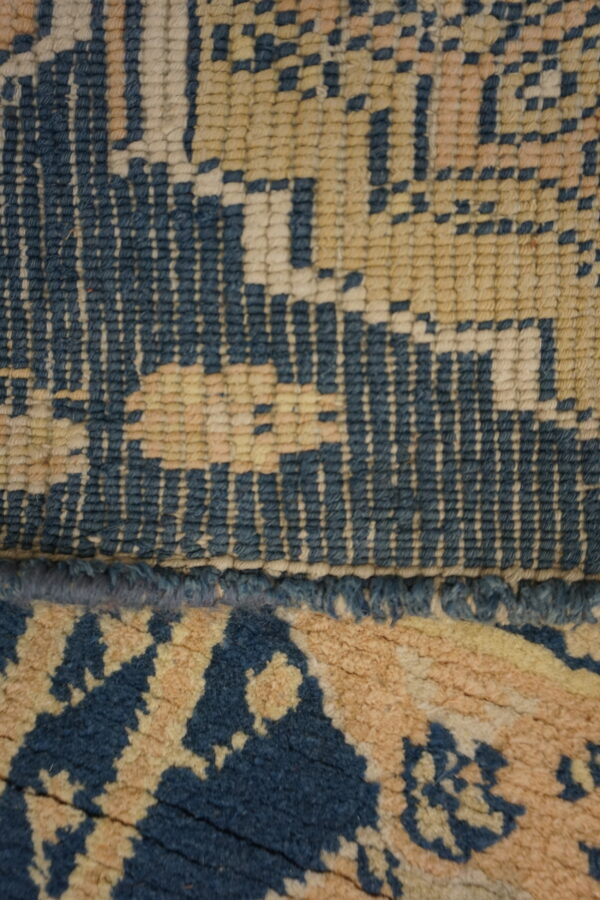Dark blue and cream patterned rug on worn wood floors next to an inventory tag and a black shoe.