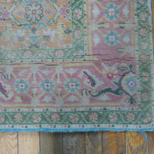 Heavily distressed traditional rug in muted pink and green patterns rests on vertical wood flooring.