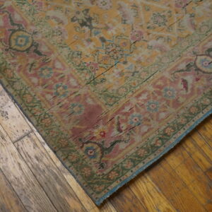 A distressed floral rug in pink, yellow, and green sits on rustic, wide plank wood floors.