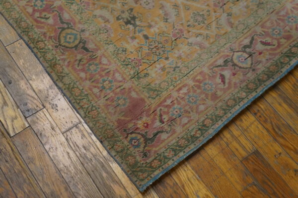 A distressed floral rug in pink, yellow, and green sits on rustic, wide plank wood floors.