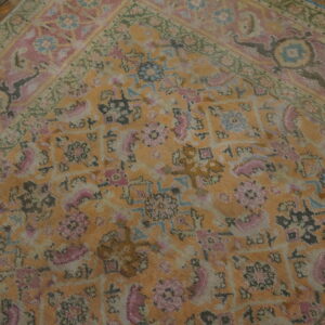 Faded orange and pink traditional rug with green border details shown on dark hardwood planks.