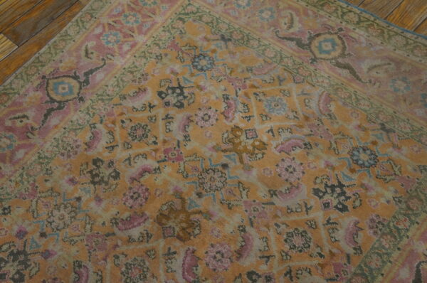 Faded orange and pink traditional rug with green border details shown on dark hardwood planks.
