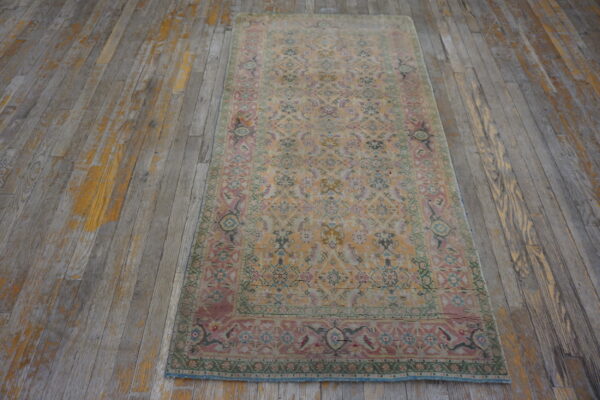 Faded traditional runner in apricot, pink, and green rests on distressed gray and yellow hardwood flooring.