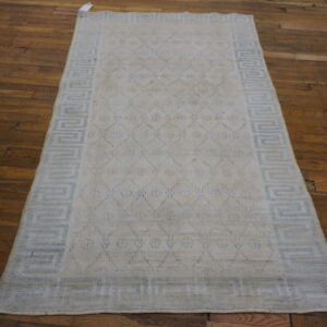 Rectangular cream rug with blue geometric diamonds and a Greek key border on dark wood floors.