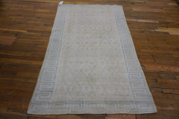 Rectangular cream rug with blue geometric diamonds and a greek key border on dark wood floors.