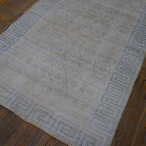 Distressed light blue and gray rug with a geometric border lies on dark wood flooring.