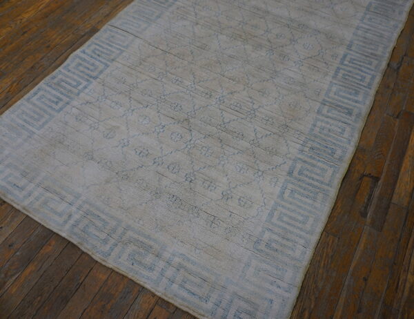 Distressed light blue and gray rug with a geometric border lies on dark wood flooring.