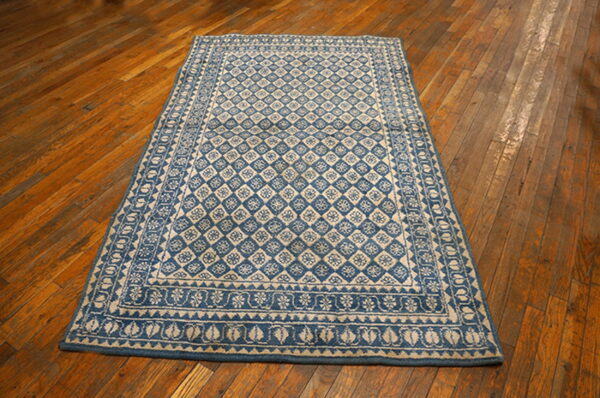 Blue and tan rug with repeating diamond and floral motifs rests on distressed hardwood floors.
