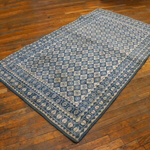 Blue and beige flatweave rug with diamond and floral patterns lies diagonally on warm wooden floorboards.