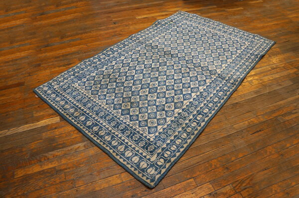 Blue and beige flatweave rug with diamond and floral patterns lies diagonally on warm wooden floorboards.