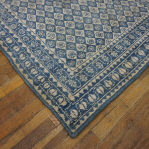 A blue and cream patterned rug corner with geometric and floral designs rests on rustic wooden plank flooring.