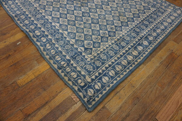 A blue and cream patterned rug corner with geometric and floral designs rests on rustic wooden plank flooring.