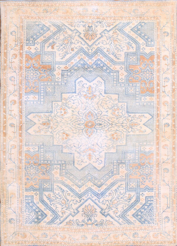 This low-pile rug features a central medallion and repeating geometric patterns in light blue, peach, and cream.