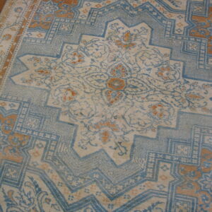 Faded traditional rug featuring light blue, cream, and rust geometric and floral patterns on wood flooring.