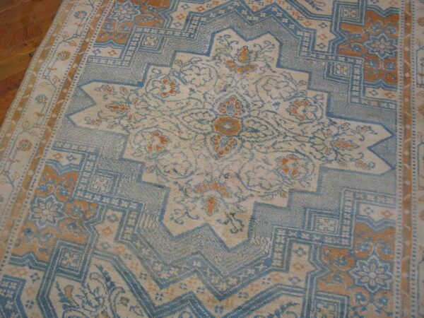 Faded traditional rug featuring light blue, cream, and rust geometric and floral patterns on wood flooring.
