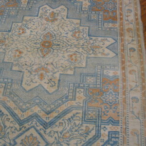 Muted blue, cream, and tan rug with intricate geometric patterns sits on hardwood flooring.