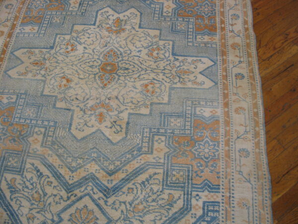 Muted blue, cream, and tan rug with intricate geometric patterns sits on hardwood flooring.