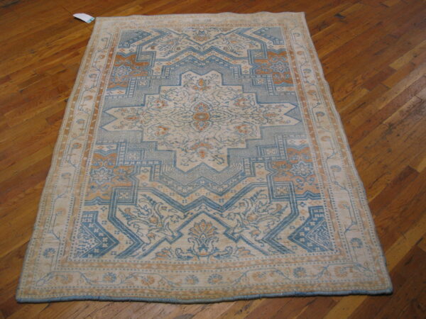 Blue, cream, and rust traditional rug with a geometric medallion pattern rests on diagonal hardwood floors.