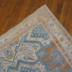 Traditional low-pile rug in cream, faded blue, and tan with geometric patterns against distressed hardwood flooring.