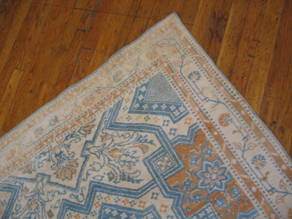 Traditional low-pile rug in cream, faded blue, and tan with geometric patterns against distressed hardwood flooring.