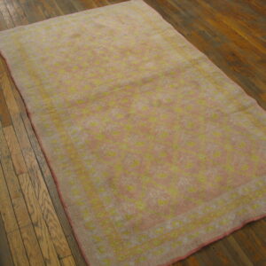 Faded pink and yellow floral rug lies on distressed dark brown hardwood flooring.