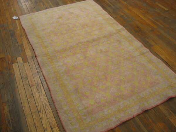 Faded pink and yellow floral rug lies on distressed dark brown hardwood flooring.