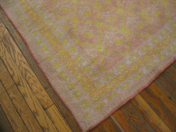 A shaggy pink and yellow patterned rug corner rests on medium-toned wood plank flooring.