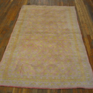 A high-pile pink rug with a yellow geometric pattern rests on dark wood planks.