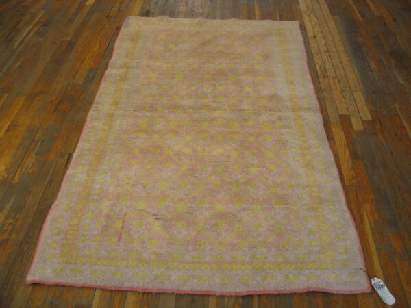 A high-pile pink rug with a yellow geometric pattern rests on dark wood planks.