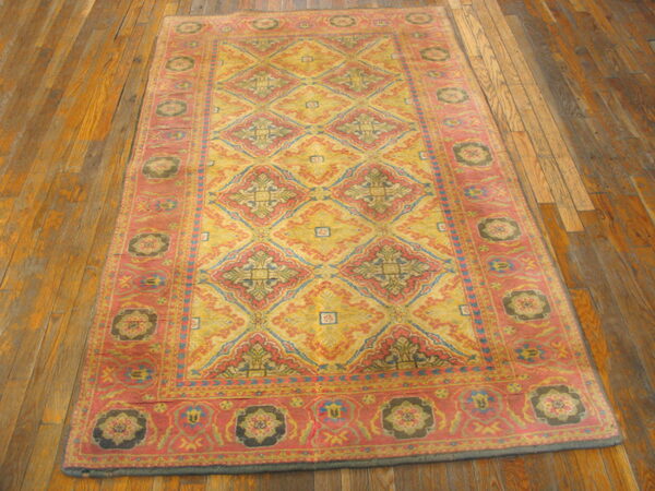 Yellow, pink, and blue patterned rug featuring geometric diamonds and floral medallions resting on distressed wood flooring.