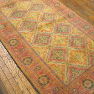 Traditional rug in coral and faded yellow featuring geometric medallions over rustic wood flooring.